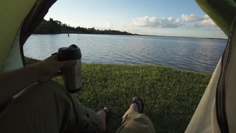 Sonnenaufgang-über-Einem-Ruhigen-See-Aus-Einem-Campingzelt-Beim-Kaffeetrinken,-Kaukasischer-Mann