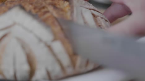 Extreme-close-up-rack-focus-of-a-knife-cutting-through-a-loaf-of-artisan-bread
