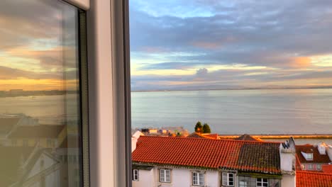 Wunderschöne-Aussicht-Auf-Den-Sonnenuntergang-Von-Einem-Fenster-An-Einem-Fluss-Mit-Traditionellen-Orangefarbenen-Dächern-Und-Einem-Unglaublichen-Himmel-In-Der-Stadt-Lissabon,-Portugal,-4k