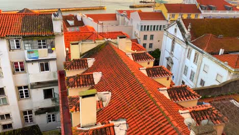 Wunderschöne-Aussicht-Auf-Den-Sonnenuntergang-Von-Einem-Fenster-Auf-Einem-Fluss-Mit-Fahrenden-Booten-Mit-Traditionellen-Orangefarbenen-Dächern-Und-Einem-Unglaublichen-Himmel-In-Der-Stadt-Lissabon,-Portugal,-4k-Nach-Oben-Geneigt