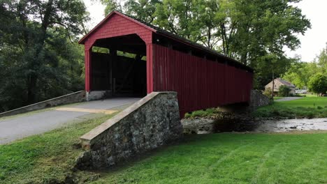 Red-covered-bridge-at-Historic-Poole-Forge-in-Narvon,-Pennsylvania-PA-USA,-aerial-push-in-shot
