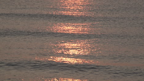 A-slow-motion-shot-of-a-stunning-red-and-golden-sunrise-reflects-on-calm-silvery-waters-as-small-waves-roll-in