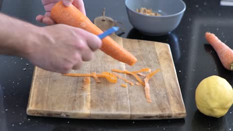 Close-up-of-peeling-a-large-carrot-over-a-wooden-cutting-board