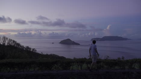 Beautiful-vista-out-towards-open-ocean-and-silhouetted-islands-at-sunrise-with-male-walking-through-frame