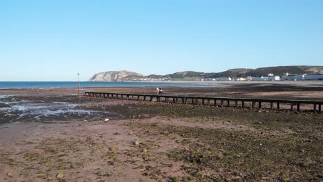 Rustic-wooden-pier-at-low-tide-with-rocks-scattered-on-the-beach,-Llandudno,-Wales