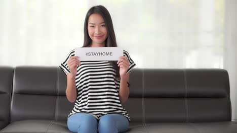 Asian-woman-wearing-casual-clothes-shows-the-written-on-paper-message-with-the-hashtag-Stay-Home