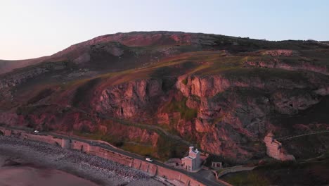 A-pink-sunset-reflects-off-the-limestone-cliffs-of-the-Great-Orme-in-Wales,-aerial-view