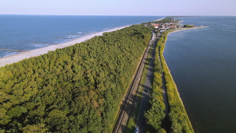 Aerial-cinematic-beautiful-straight-road-along-the-forest-between-the-bay-and-sea-waters,-Kuznica-Poland