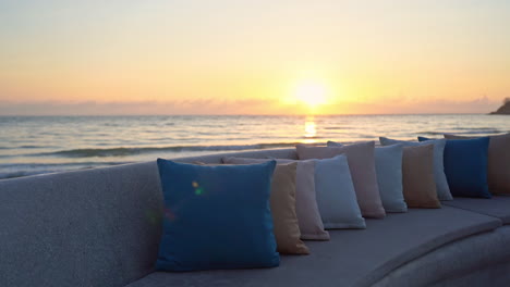 Eine-Mit-Bunten-Kissen-Ausgekleidete-Strandcouch-Wartet-Darauf,-Dass-Ein-Vorbeifahrender-Tourist-Sitzt-Und-Den-Sonnenuntergang-Am-Meereshorizont-Genießt