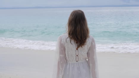 Ultra-slow-motion-shot-of-woman-with-brown-hair-in-white-dress-walking-on-beautiful-beach-looking-at-the-ocean-at-Asu-Island,-North-Sumatra,-Indonesia