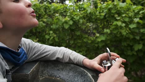 Happy-young-Caucasian-male-drinking-fresh-water-from-outdoor-fountain-faucet