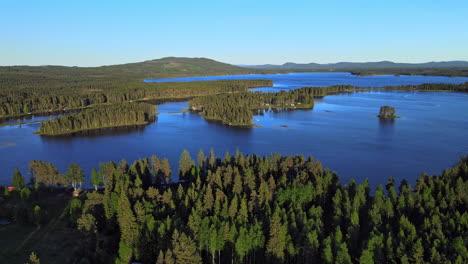Panorama-Of-Lush-Forest-By-The-Calm-River-In-Vansbro-Municipality,-Dalarna-County,-Sweden-With-Blue-Sky-In-The-Background