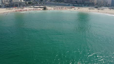 Beautiful-drone-shot-of-the-water-while-flying-towards-land-to-reveal-the-popular-tourist-attraction-of-Tel-Aviv-beach