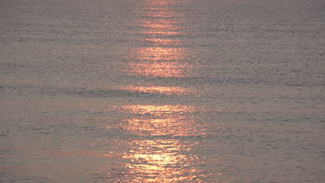 Ein-Atemberaubender-Roter-Und-Goldener-Sonnenaufgang-Spiegelt-Sich-Auf-Dem-Ruhigen,-Silbrigen-Wasser-Wider,-Während-Kleine-Wellen-Hereinrollen