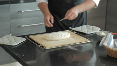Ein-Bäcker-In-Einer-Sauberen,-Modernen-Küche-Ritzt-Rohes-Handwerkliches-Brot,-Damit-Es-Sich-Während-Des-Backens-Ausdehnen-Kann
