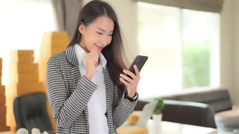 Successful-Young-Asian-Businesswoman-in-Office-Swiping-For-Great-News-on-Mobile-Phone