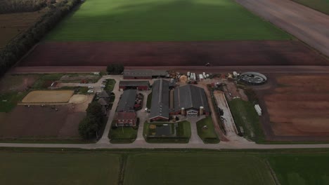 Aerial-descend-and-tilt-showing-a-Dutch-agriculture-farm-with-sunlight-hitting-the-patches-of-meadow-and-crop-farmland-around-the-constructions-pertaining-the-business