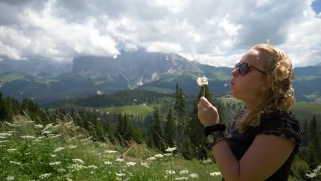 Super-Slow-Mo-of-a-Blonde-Girl-blowing-a-dandelion-flower-in-the-wind-in-a-beautiful-nature-setting-outdoor-in-the-summer,-Val-gardena,-Alpe-si-Siussi