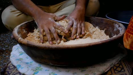 man-kneading-flour-dough-with-both-hands-in-a-wooden-plate-placed-on-cotton-cloth