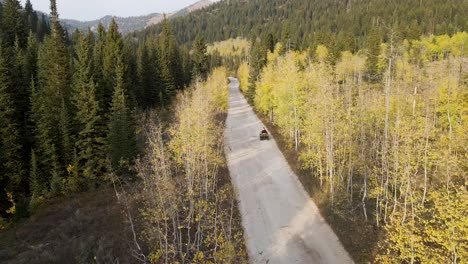 All-terrain-vehicle-ATV-driving-on-country-road-through-mountain-forest,-aerial