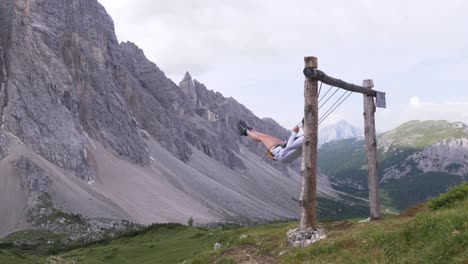 Blonde-Tourist-girl-on-a-swing-in-the-Mountains-in-the-Italian-Alps,-Alleghe,-Dolomite-near-Refugio-Tissi,-Italy
