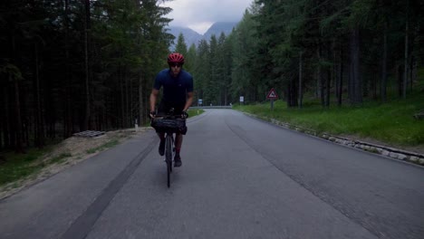 Man-in-sporty-outfit-cycles-through-the-forest-at-a-high-speed-on-an-early-morning-in-the-Italian-mountains,-Dolomiti
