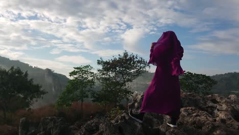 Islamic-woman-wearing-purple-burqa-stands-on-rocky-summit-looking-at-landscape