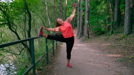A-close-up-view-of-a-caucasian-lady-is-in-sportswear-doing-stretching-exercises-in-a-park-surrounded-by-woods