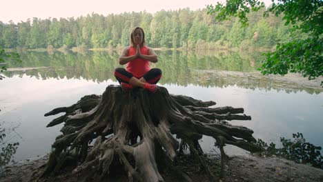 A-caucasian-woman-in-sportswear-sitting-on-a-tree-stump-and-practicing-yoga