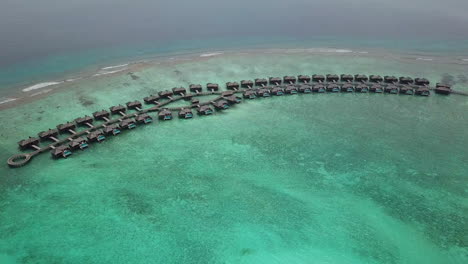 Wide-tilting-downward-drone-shot-of-private-villas-over-the-turquoise-water