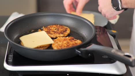 Close-up-of-adding-cheese-to-chicken-burgers-while-frying-on-a-hotplate