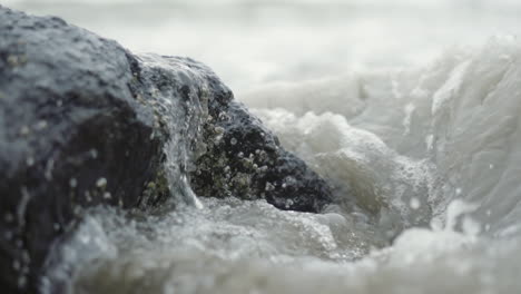 Ocean-waves-crashing-over-barnacle-covered-rock-on-beach-in-slow-motion