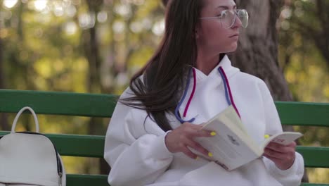 Girl-with-glasses-reading-a-book-on-a-bench-in-a-peaceful-environment-in-a-park