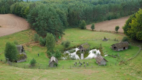 Old-Barns-With-Large-Stone-Circles-Enclosed-By-Rustic-Fence-In-Lush-Green-Village-Settlement-In-Piaszno,-Pomorze-In-Northern-Poland---Wide-Shot