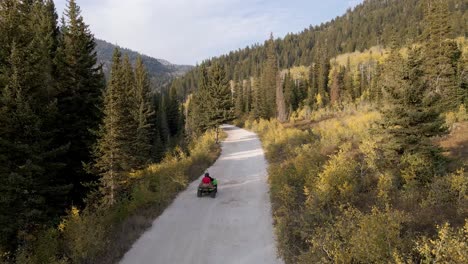 All-terrain-vehicle-ATV-on-mountain-backcountry-road,-rear-aerial-view