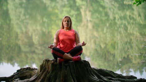 A-woman-in-sportswear-practicing-breathing-yoga-on-a-log-over-the-forest-lake