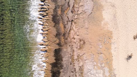 Aerial-overhead-drone-clip-over-a-beach-with-waves-crushing-the-rocks-on-the-shore-in-Kavala,-Macedonia,-Greece