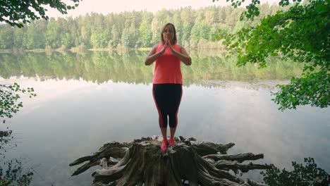 A-caucasian-woman-in-sportswear-standing-on-a-tree-stump-and-practicing-yoga