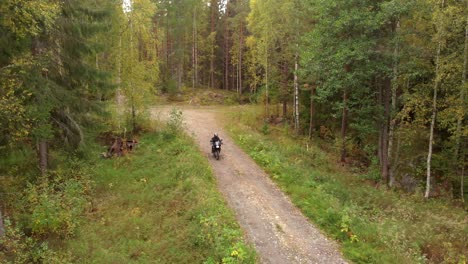 Motorcyclist-driving-towards-the-camera-on-a-small-gravel-road-in-the-forest