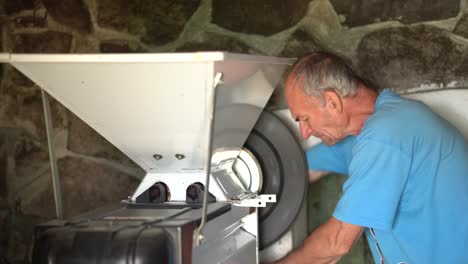 Older-caucasian-wine-grower-milling-grapes-with-hand-grape-crusher-machine-in-wine-cellar