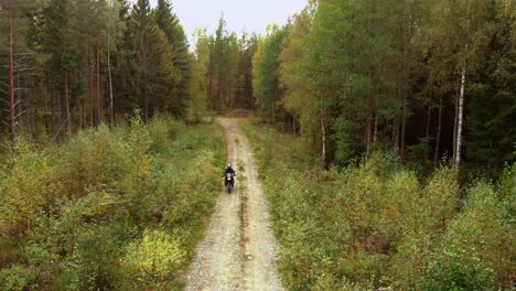 Motorcyclist-driving-towards-the-camera-on-a-small-gravel-road-in-the-forest