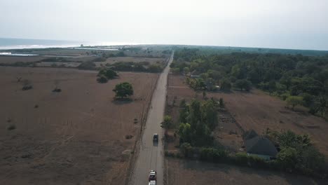 Drone-aerial,-4x4-cars-driving-through-highway-next-to-the-sand-towards-the-beach-in-monterrico,-Guatemala,-Central-america