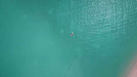Rising-drone-shot-from-man-laying-on-surf-board-or-paddle-board-in-ocean
