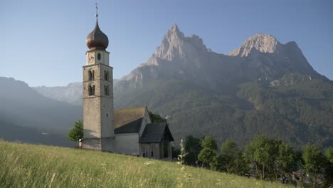 Perfektes-Altes-Kirchengebäude-In-Einem-Grünen-Tal-In-Den-Bergen-An-Einem-Sonnigen-Tag-Gleitschuss,-St.-Ulrich,-Südtirol,-Italien