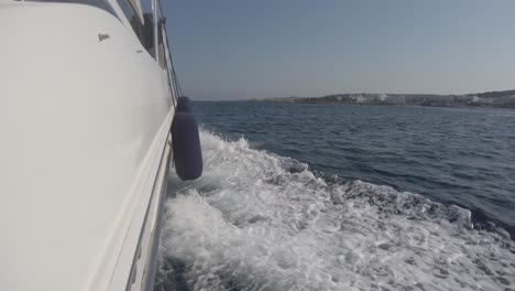 Blick-Von-Der-Seite-Einer-Yacht,-Die-Mit-Dem-Ufer-In-Der-Ferne-Durch-Mediterrane-Gewässer-Rast