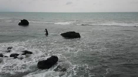 Fisherman-trying-to-catch-fish-on-rocky-shore-of-West-Java-between-ocean-waves