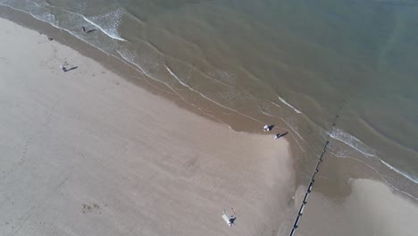 Sunny-aerial-view-looking-down-over-golden-sandy-beach-with-tourists-walking-below-tilt-up-across-ocean-tide