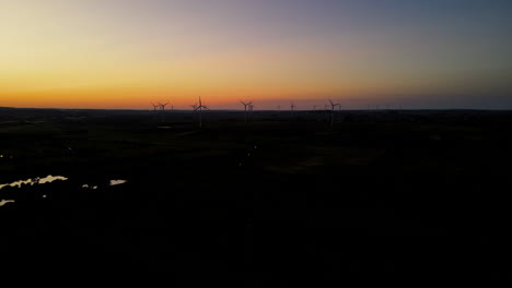Aerial-view-of-dark-silhouetted-wind-turbine-farm-against-beautiful-sunset-on-horizon