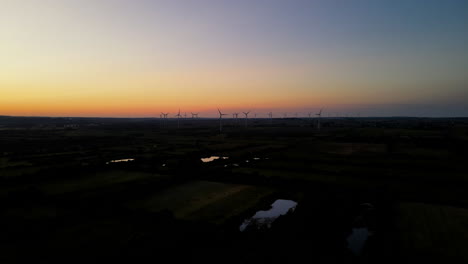 Wind-energy-farm-working-on-sunset-in-Puck-city,-Pomorskie-zone,-Poland,-drone-pull-out-motion