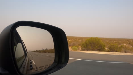 Driving-down-a-desert-highway-while-looking-in-the-side-view-mirror-of-the-car